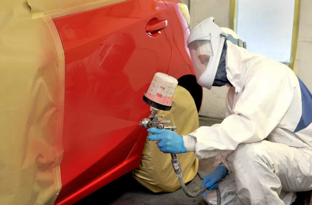 Car paint technician spray painting red car