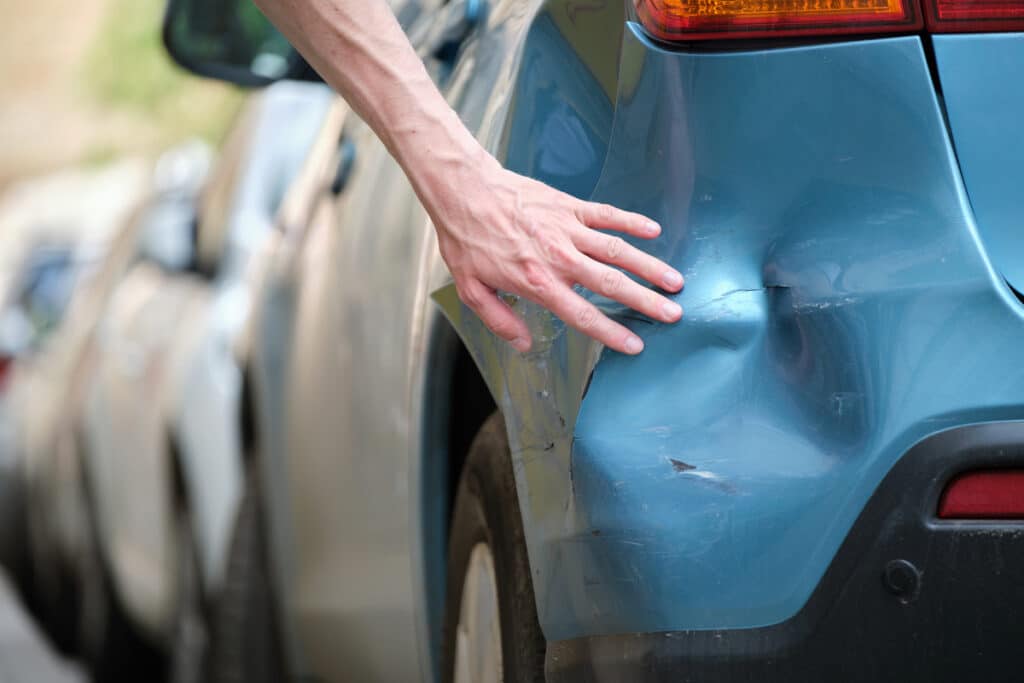 Driver's hand examining dented car with damaged fender